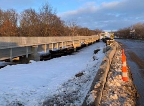 An image of a new bridge next to the older bridge, taken from the snowy bank of the river.