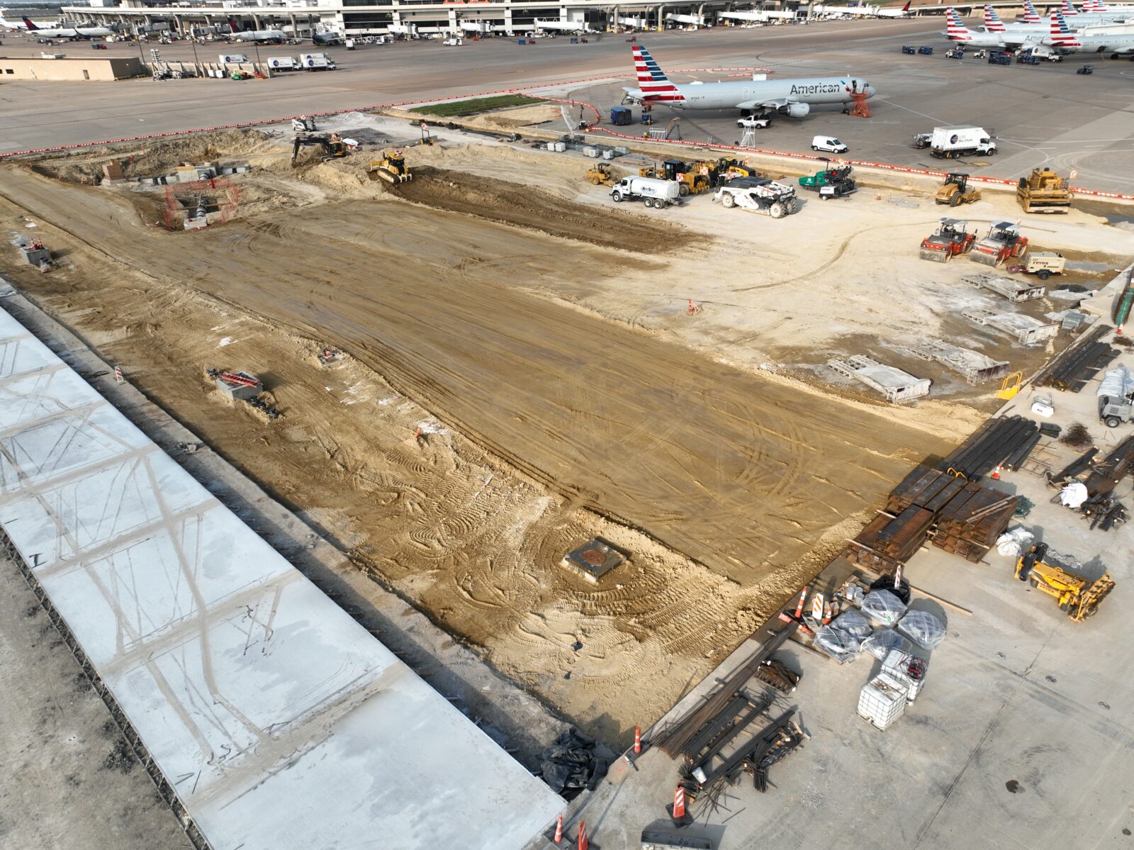 Image of an area on DFW airport pavement under construction, with airplanes in the background.