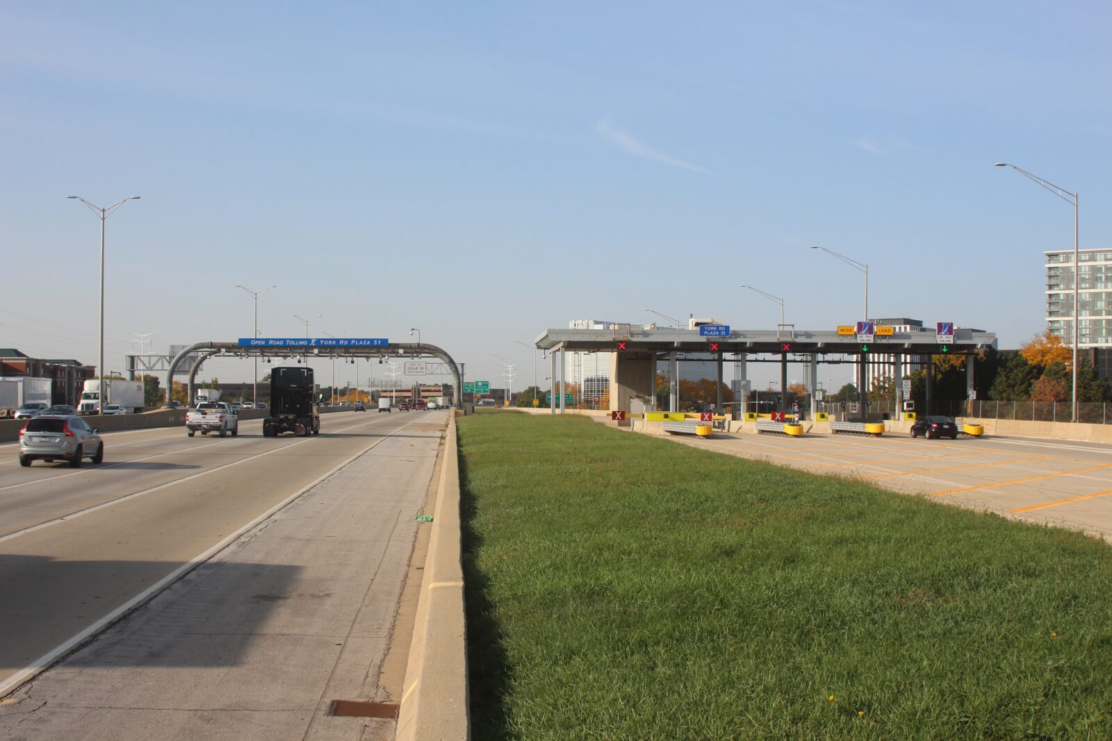 An image of a toll road. To the right is a five lane toll booth, with two lanes open. To the left is a structure spanning the highway with cameras for automatic tolling.