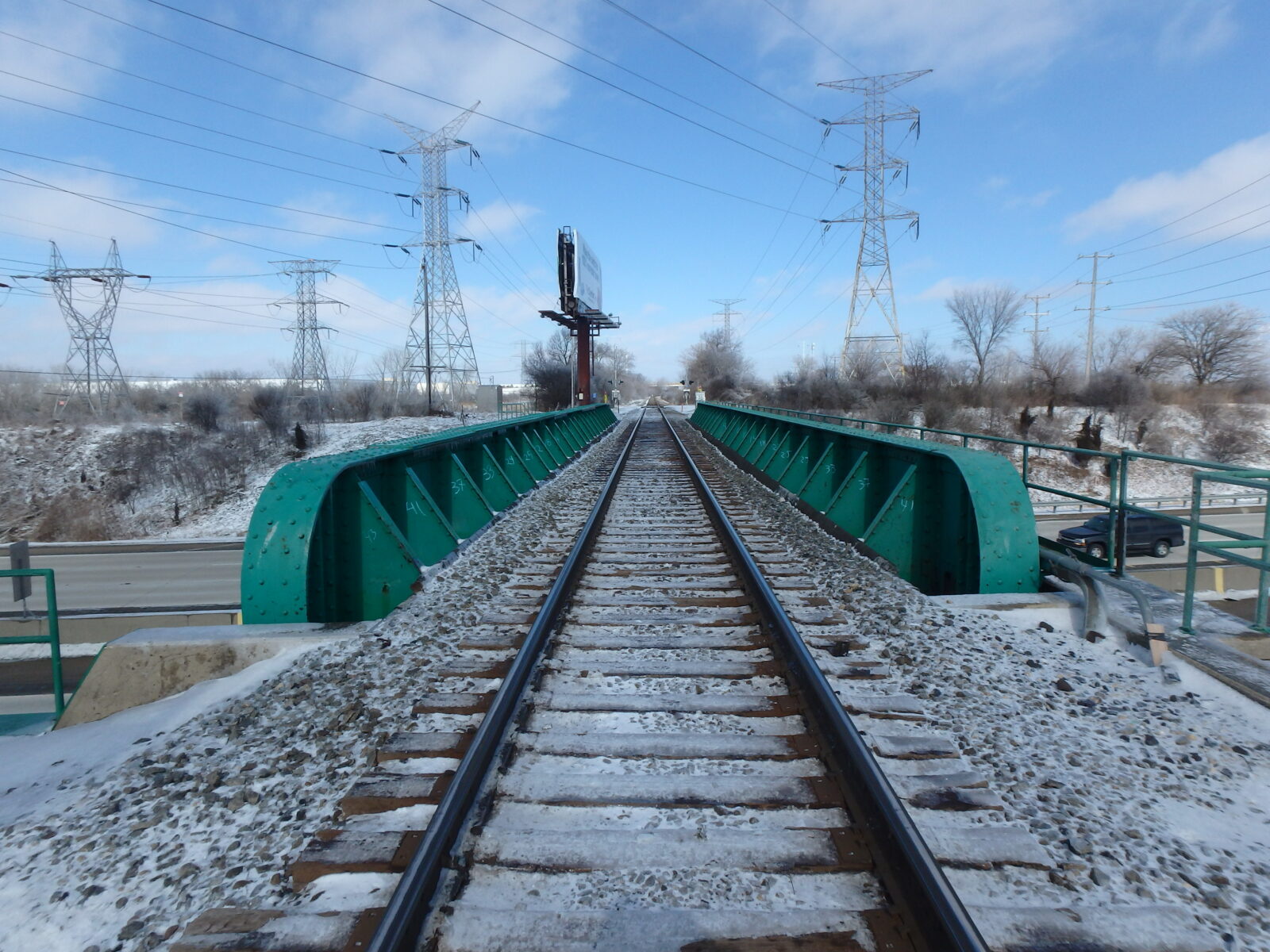 An image of a snowy rail bridge over a highway, taken from the tracks.