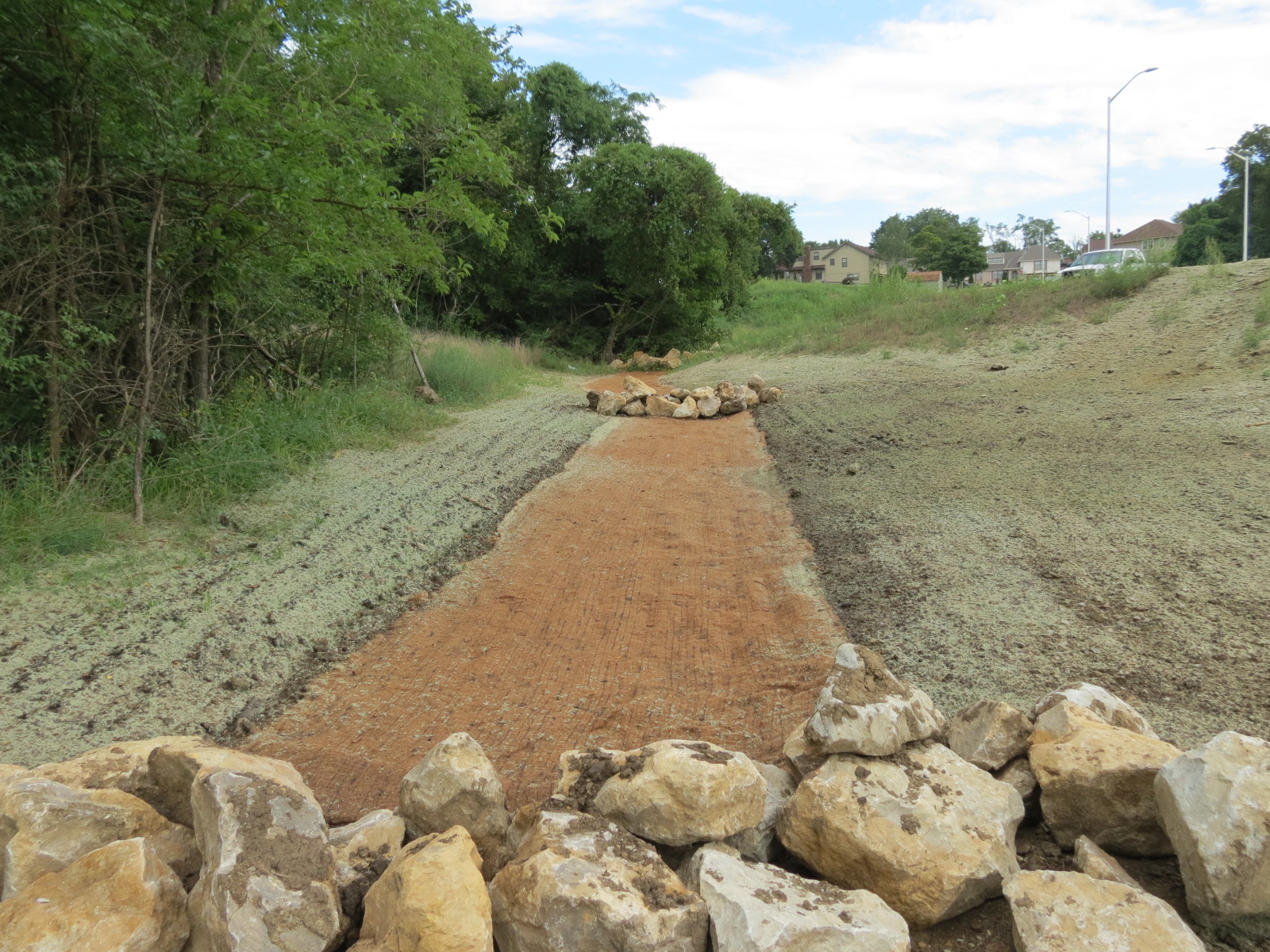 Image of a ditch near a road, with rocks periodically along a strip of red soil