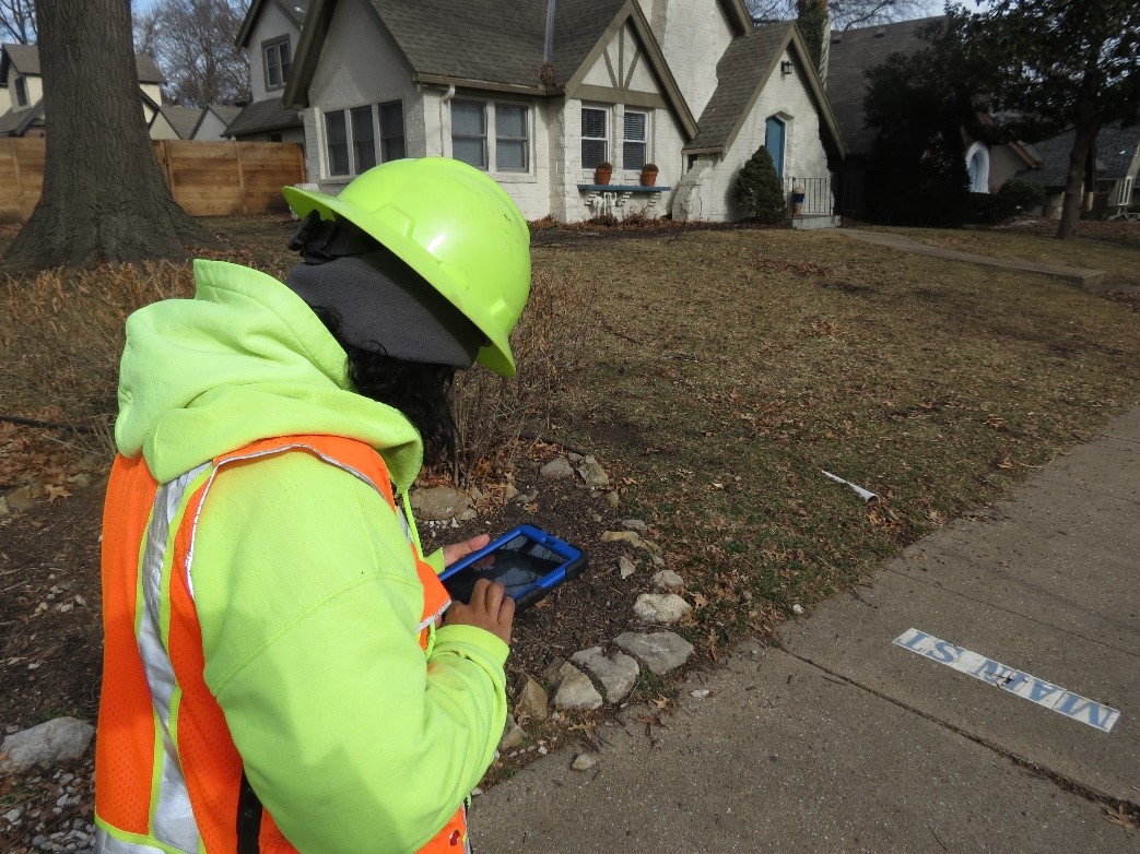 A person in hi-vis clothing looks at a phone, inspecting sidewalk