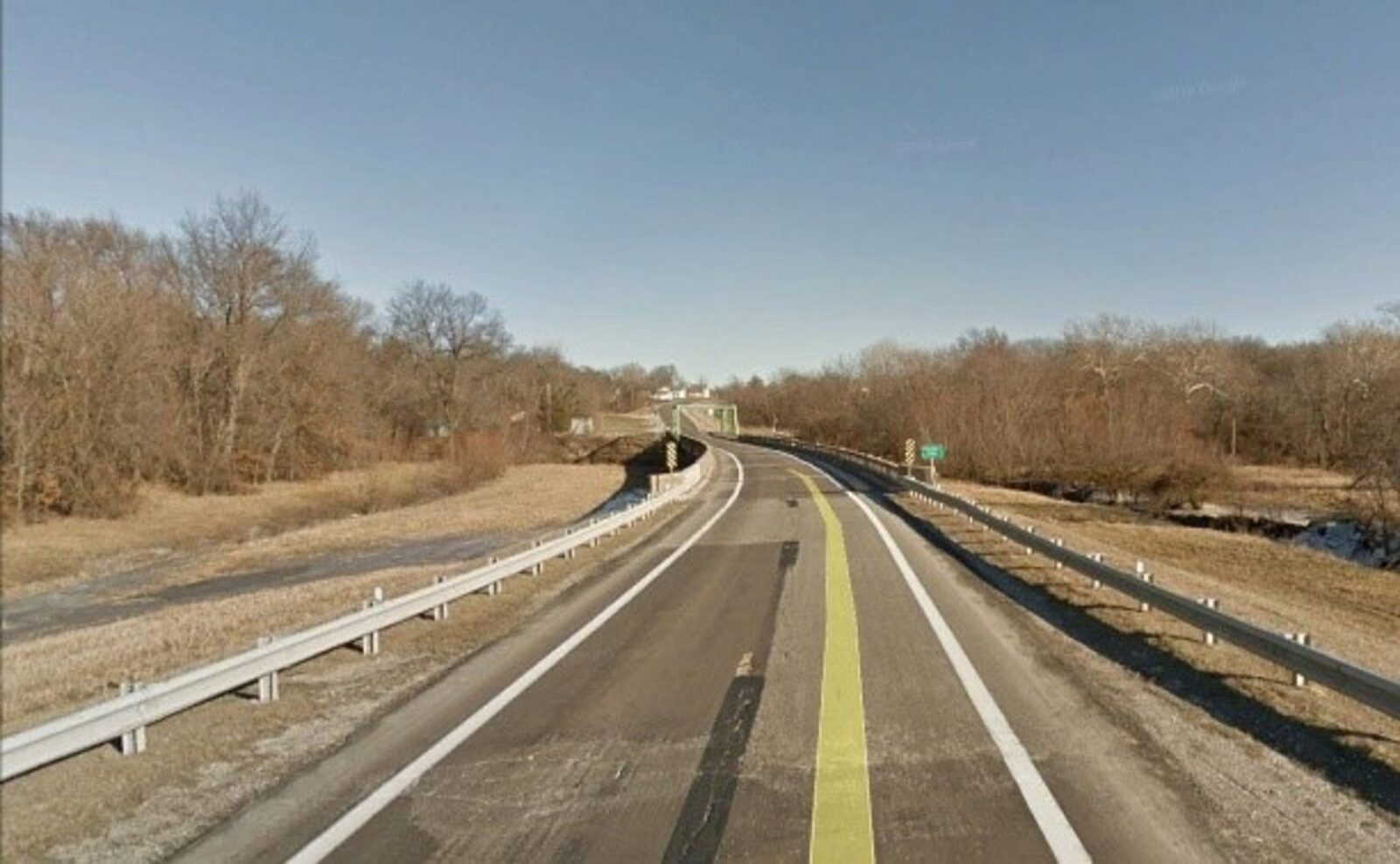 An image of a bridge over a small river, taken from the road approaching the bridge.