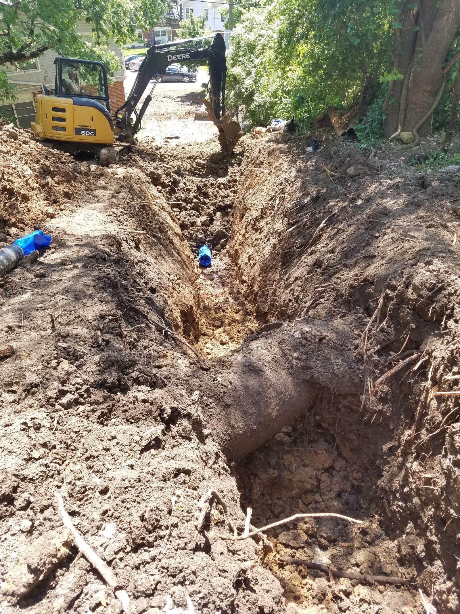 An image of an excavated ditch, with construction equipment in the background and a pipe in the foreground.