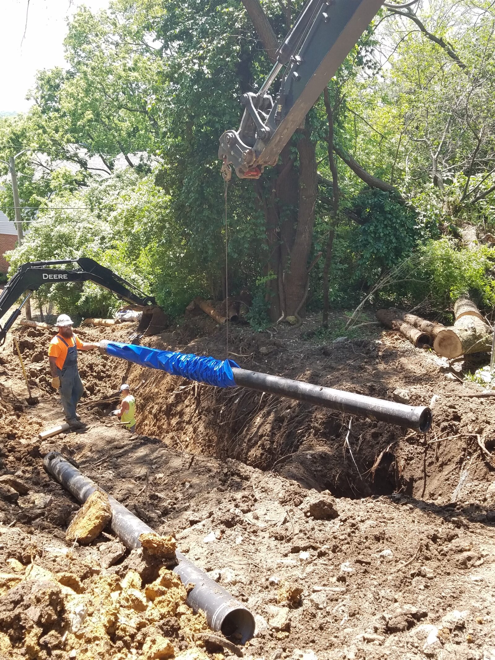 An image of a crane lowering a length of pipe into an excavated ditch, guided by a construction worker.