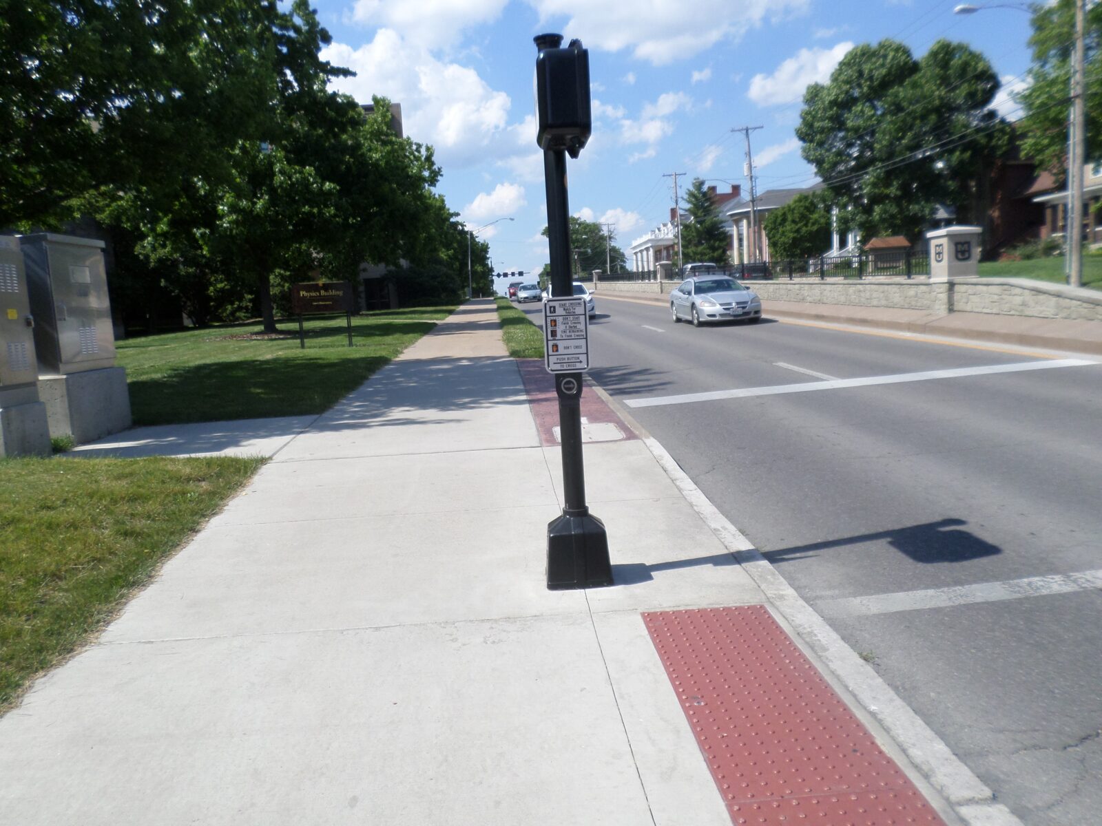 An image of a post with a pedestrian push-button and signal head on it, on sidewalk next to a road.