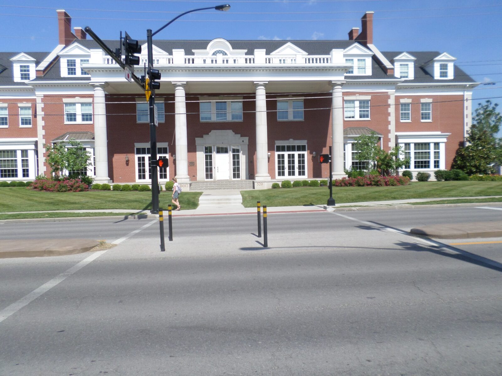 An image of a pedestrian crosswalk at an intersection. There is a gap in the central median to allow pedestrians a flat crosswalk, with bollards in it to prevent vehicles entering that space.