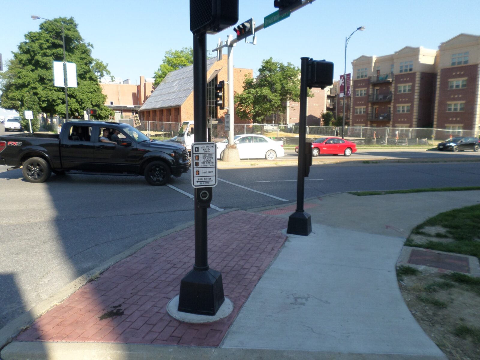 An image of two posts in the sidewalk at the corner of an intersection. Both have a pedestrian push-button and signal head on them.