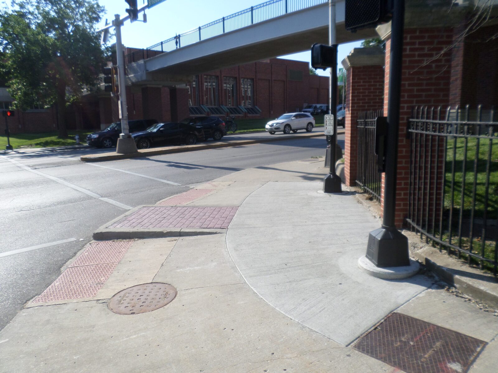An image of a corner of an intersection. There are two poles with pedestrian push-buttons and signal heads visible. There are also two ADA ramps cut into the curb.