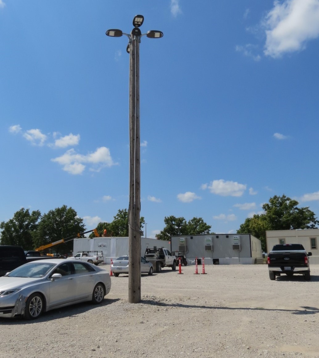 An image of a light post in a gravel parking lot, with logistics buildings and construction equipment in the background.