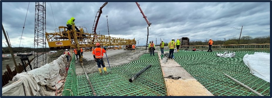 An image of a bridge under construction. Workers are laying concrete with construction equipment.