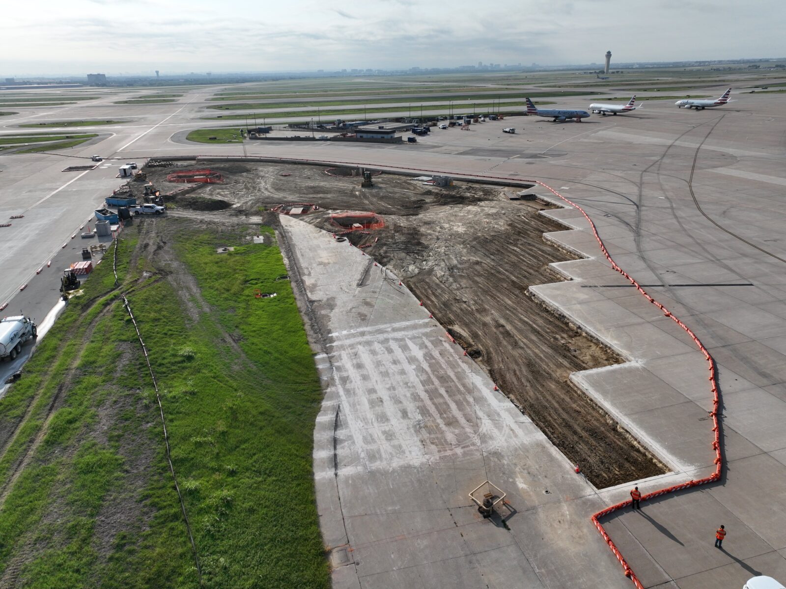 An image of a section of airport infield under construction. There are planes and runways visible in the background.