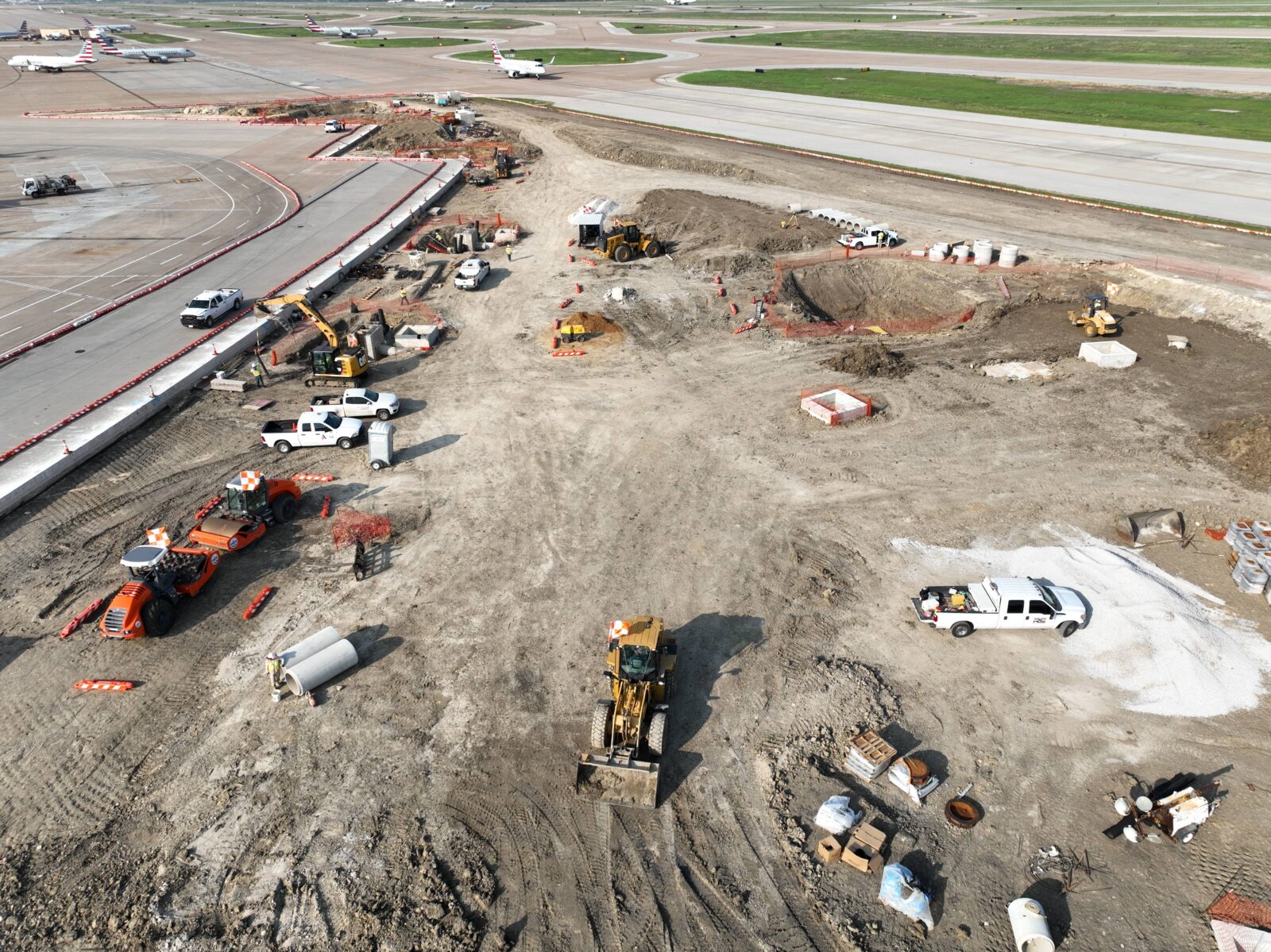 An image of a section of airport infield under construction. There are runways and planes visible in the background.